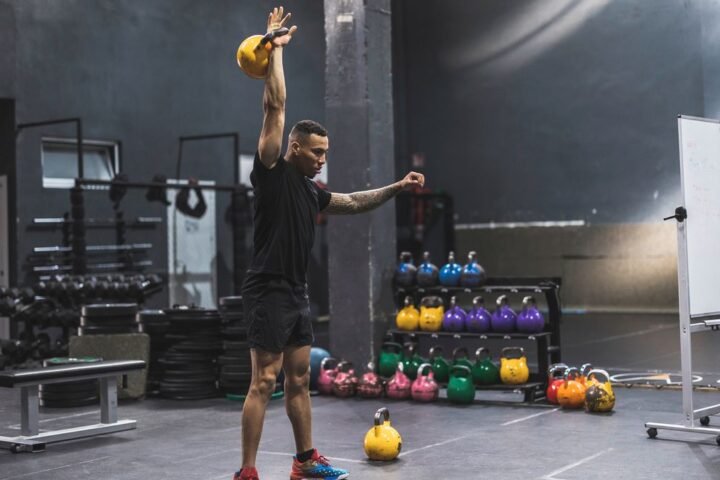 Man in gym holds kettlebell above his head