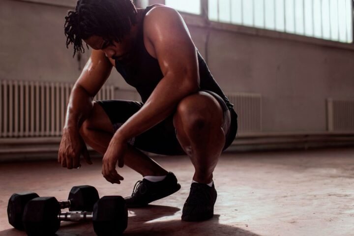 Man crouches over a pair of dumbbells
