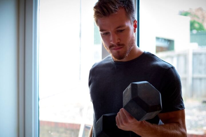 Man performs biceps curl with a dumbbell at home