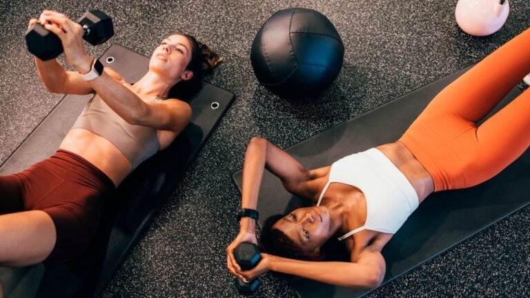 Two women lying on the floor lowering a dumbbell behind their heads