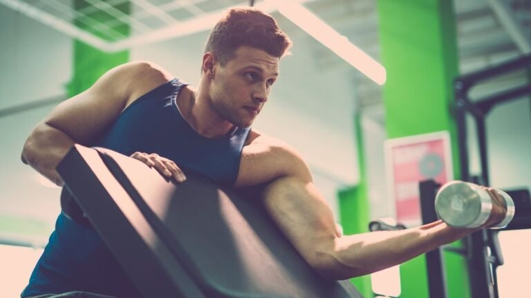 Man performing single-arm dumbbell preacher curl in gym